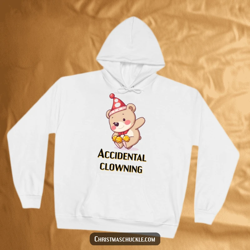 Funny hoodie graphic of a bear in a clown hat and jingle bells, comically tripping over its feet, designed for ultimate cozy humor.