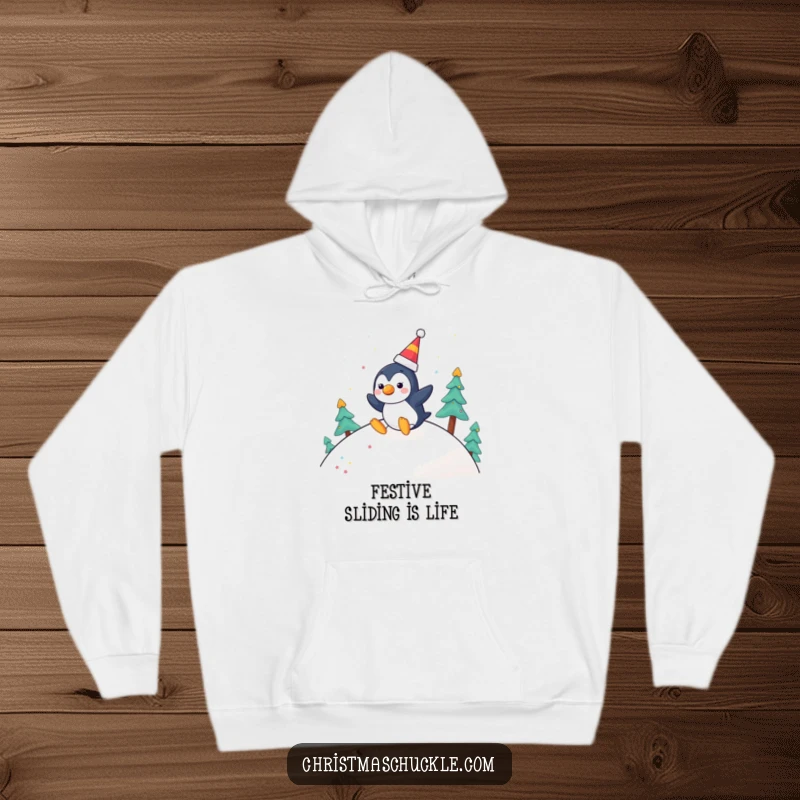 Funny hoodie graphic of a cheerful penguin wearing a clown nose, joyfully sliding down a festive hill, designed for cozy winter vibes.