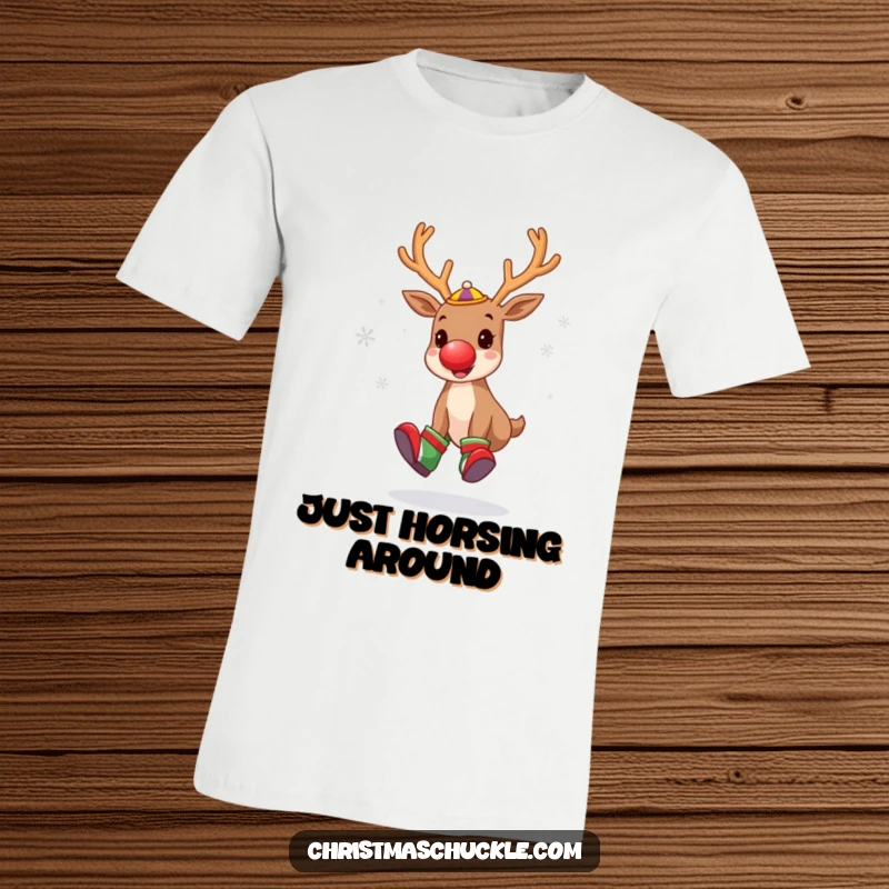 Funny t-shirt showcasing a cute reindeer as a clown, complete with a red nose and oversized shoes, juggling snowflakes with a comical stance.
