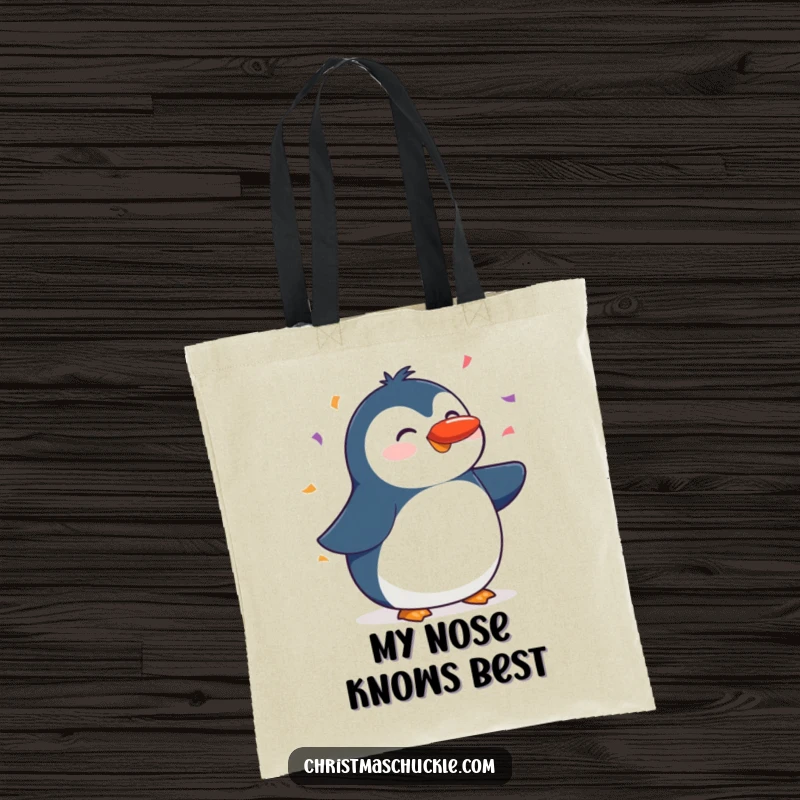 Funny tote bag featuring a happy penguin balancing a red nose on its beak amidst a cascade of confetti, practical and cute.